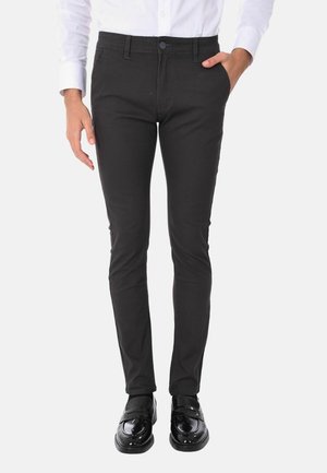 Pantaloni neri slim-fit realizzati in tessuto testurizzato, con chiusura a bottoni e tasche laterali, indossati con Mocassini neri lucidi e una camicia bianca.