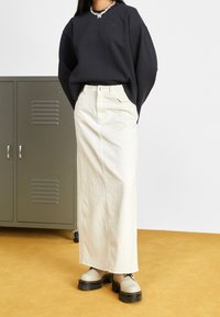 Black oversized sweatshirt, cream long denim skirt, and beige chunky-soled shoes. Notable details include a round neckline and functional pockets.