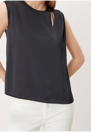 Ärmellose schwarze Bluse mit kleinem Ausschnitt-Detail am Schlüsselbein, getragen zu weißen Hosen, dargestellt vom mittleren Oberkörper bis zu den Hüften.