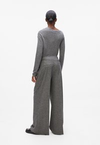Grauer Strickpullover und weite Hose aus strukturiertem Stoff. Das Outfit hat eine lockere Passform und einen schmalen Bund.