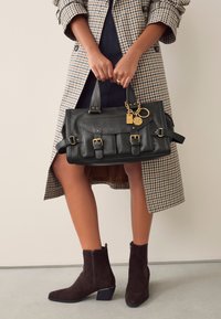 Melna ādas soma ar zelta detaļām, trim priekšējām kabatām un ķēdes aksesuāru. Soma ir ar strukturētu dizainu un izturīgiem rokturiem.