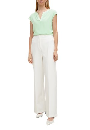 Woman wearing a light green short-sleeve blouse tucked into high-waisted wide-leg white trousers and white pointed-toe heels.
