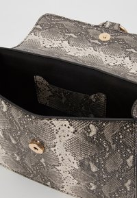 Černobílá kabelka s texturou hadí kůže a elegantním designem, s zlatým cvokem na zavírání a černou kapsou uvnitř.