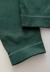 Tume roheline fliiskanga pinda soonikkoes varrukate äärega. Tekstuur on sile ja õmblused korrektsed, millel on peen vertikaalne muster.