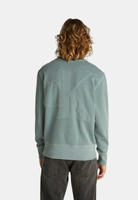 Felpa azzurra con collo tondo, con grande logo "CK" ricamato sul retro, realizzata in tessuto morbido e con polsini e orlo a costine.