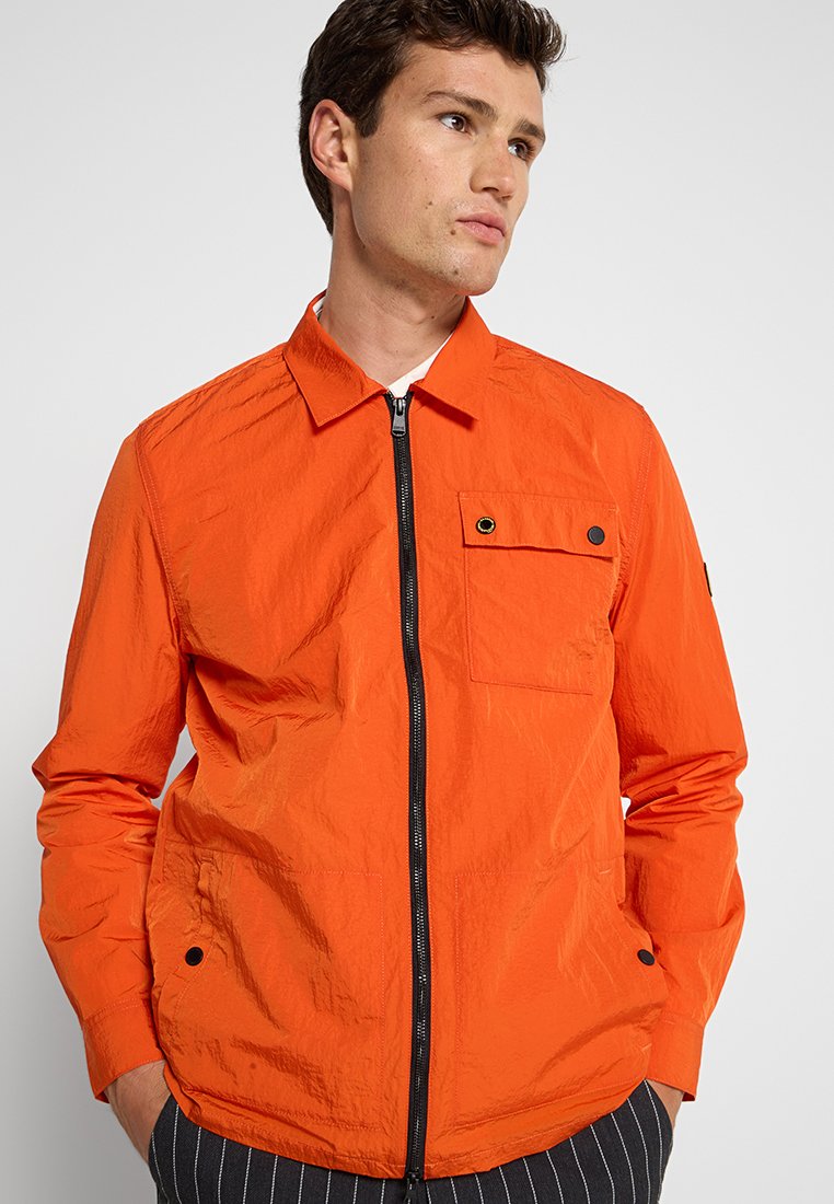 Orangene, leichte Jacke mit Reißverschluss und Druckknopftasche sowie einem strukturierten Kragen. Verfügt über eine zerknitterte Textur und schwarze Hardware-Akzente.