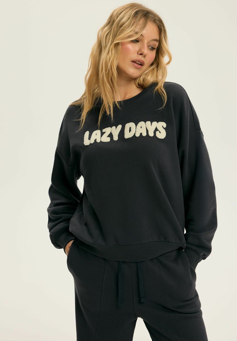 Navy Sweatshirt mit dem Aufdruck "LAZY DAYS" in strukturierter cremefarbener Schrift, Rundhalsausschnitt, lockere Passform und Rippbündchen, kombiniert mit passenden Jogginghosen.
