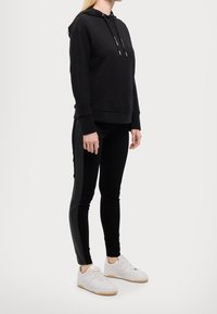 Felpa nera trapuntata con lacci, abbinata a leggings neri aderenti con pannelli laterali. Indossata con sneaker bianche e suole in gomma.