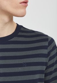 Námořnicko-modré a šedé pruhované tričko, bavlněný materiál, kulatý výstřih, malá vyšívaná značka na hrudi, těsně přiléhající k tělu.