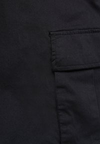 Czarna tkanina o gładkiej teksturze, z naszytą boczną kieszenią na klapę. Materiał to denim, z czystym wykończeniem i bez widocznych wzorów.