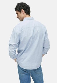Chemise boutonnée bleu clair à manches longues, coupe décontractée, détail de empiècement au dos, associée à un jean en denim bleu.
