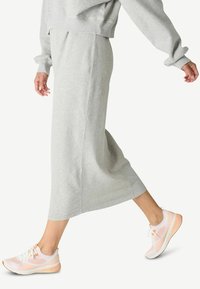 Falda de jersey gris claro, a la altura de la rodilla, con una textura suave. Combinada con zapatillas deportivas de color rosa claro y blanco que presentan un diseño de malla.