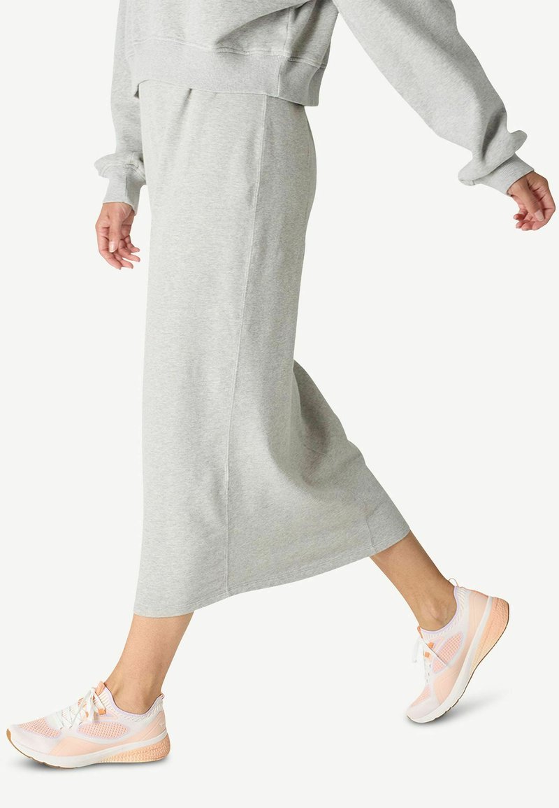 Falda de jersey gris claro, a la altura de la rodilla, con una textura suave. Combinada con zapatillas deportivas de color rosa claro y blanco que presentan un diseño de malla.