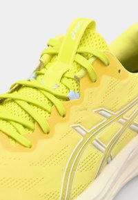 Baskets de sport jaunes avec une tige en mesh respirante, un renfort au niveau des orteils, un système de laçage proéminent et des accents de marque blancs. Semelle plate.