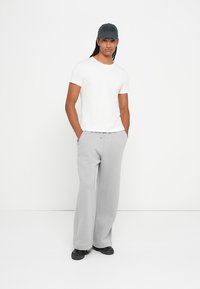 Hvid t-shirt med korte ærmer, grå sweatpants med snøre og sorte sneakers. Kappen er mørkegrå med broderede detaljer.
