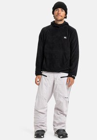 Zwarte fleece pullover met een capuchon, voorzak, gecombineerd met lichtgrijze sneeuwbroeken met ritszakken en zwarte accenten.