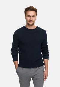 Marineblau gestrickter Pullover mit rundem Halsausschnitt und langen �Ärmeln, kombiniert mit hellgrauen Hosen. Lockerer Schnitt mit gerippten Bündchen.