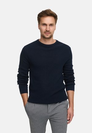 Navy blue textured sweater with a round neckline and long sleeves, paired with light gray trousers. Relaxed fit with ribbed cuffs.