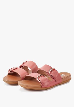 Pink slide sandals with two wide straps, featuring metallic buckles. Smooth leather upper on a cushioned tan sole with rounded edges.