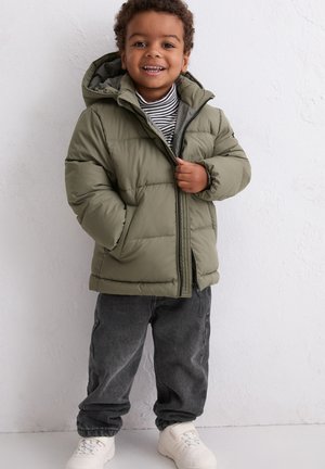 Olive green puffer jacket with a hood, front zipper, and quilted design; worn over a striped t-shirt and paired with dark jeans and white sneakers.