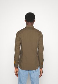 Oliwkowa koszula z długim rękawem i kołnierzykiem, z pomarańczowymi akcentami przy mankietach. Wykonana z gładkiego materiału, dopasowany krój o prostym cięciu.