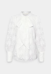 Vit blus med intrikat spetsdesign, hög hals med rosett, långa puffärmar och knäppte manschetter. Texturerad och delikat look.