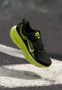 Scarpa da corsa nera e giallo neon con tomaia testurizzata, curve distintive e marchiatura prominente, caratterizzata da una suola ammortizzata e lacci.