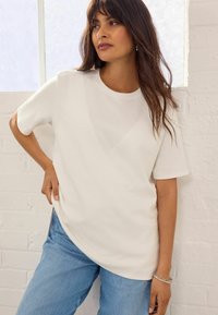 Witte katoenen T-shirt met een relaxte pasvorm, korte mouwen en een ronde halslijn, gecombineerd met lichtblauwe denimjeans. Eenvoudig ontwerp, zonder patronen.