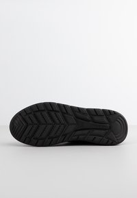 Suola di scarpa in gomma nera con motivi tessurizzati, impugnature rialzate e tacco curvo per trazione e supporto.