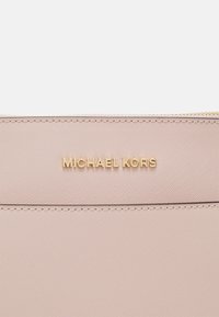 Roze leren pouch met textuur, gouden "Michael Kors" logo, ritssluiting en gestikte details langs de randen.