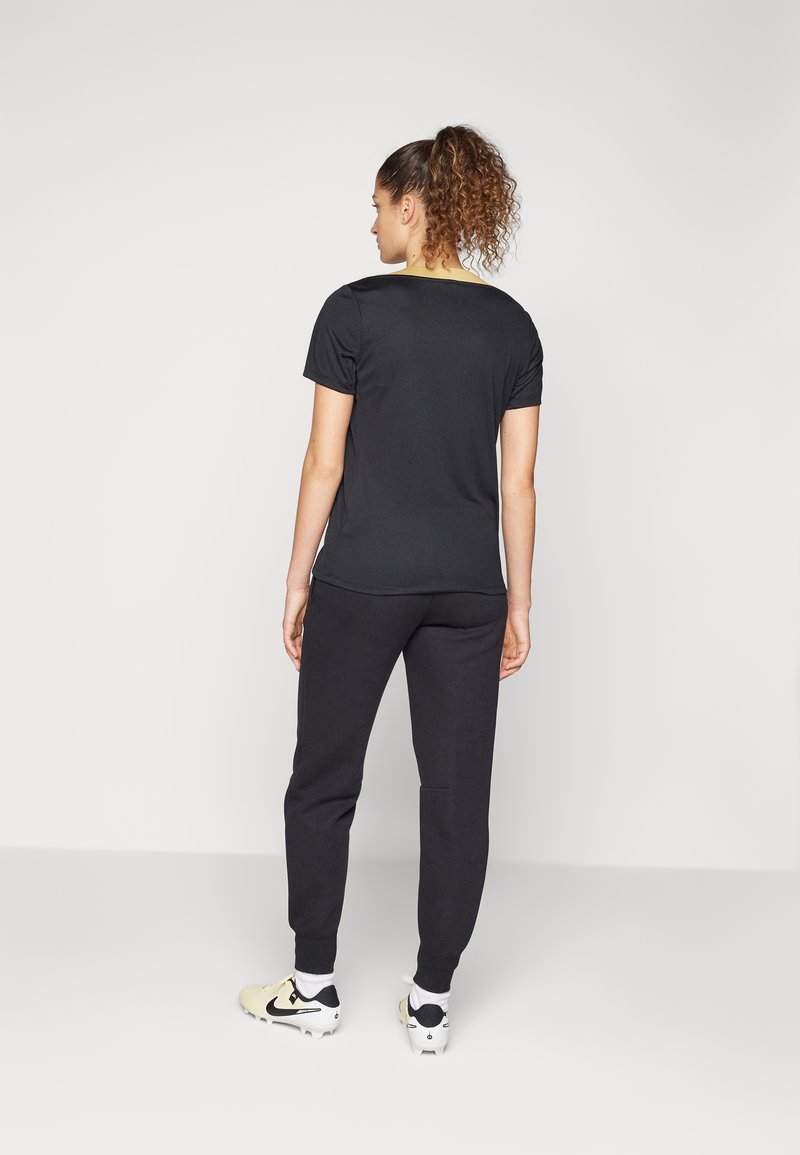 Maglietta nera in cotone a maniche corte con scollatura rotonda, abbinata a pantaloni felpati neri; l'abbigliamento ha una vestibilità comoda e una texture liscia.