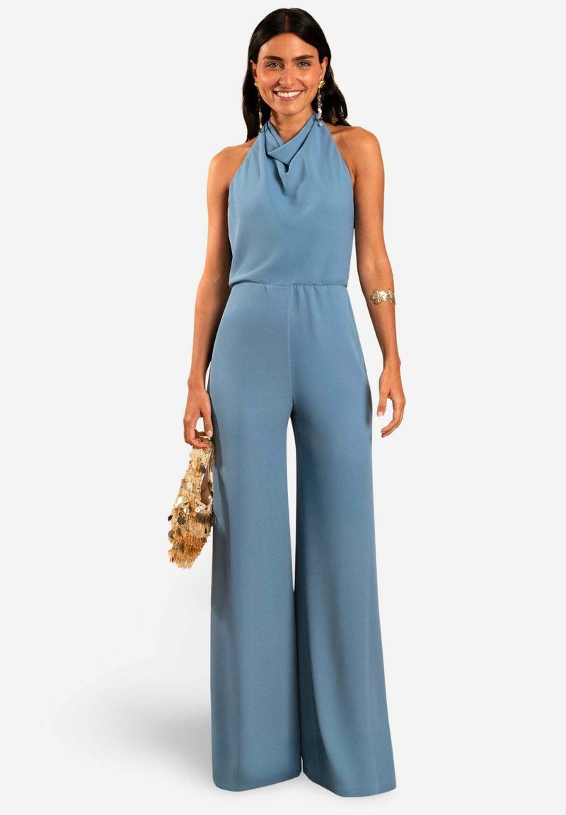 Jumpsuit de color azul claro con escote halter drapeado y diseño de pierna ancha. Presenta una tela suave y una cintura ajustada. Los accesorios incluyen un bolso texturizado.