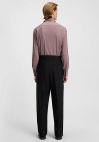 Langärmliges Hemd in Hellrot mit dezentem Muster, kombiniert mit schwarzen maßgeschneiderten Hosen mit Gesäßtaschen und einem Reißverschlussdetail.