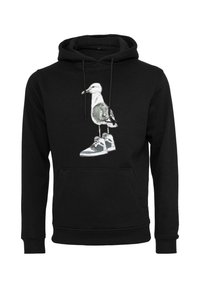 Hoodie noir avec un graphisme d'une mouette se tenant sur une paire de baskets grises au centre de l'avant.