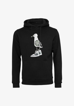 Mustat hupparit, joissa on kuva lokista, joka seisoo harmaiden lenkkarien päällä etu keskellä.