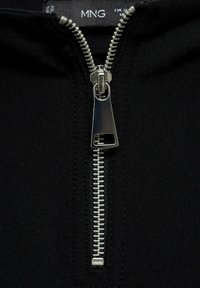 Tissu noir zippé avec une fermeture éclair en métal argenté. La fermeture éclair possède une tirette rectangulaire et des rangées de petites dents sur toute sa longueur.