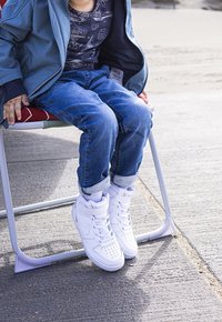 White high-top sneakers with perforated toe, laces, and padded ankle support. Worn with rolled-up blue jeans and a gray shirt.