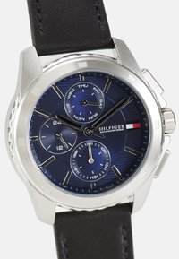 Reloj de acero inoxidable con esfera azul, correa de cuero, tres subesferas y acentos plateados. Cuenta con indicadores de día y fecha.