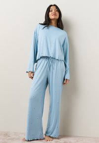 Lyseblåt loungewear-sæt med en cropped, langærmet top med flæsekant og løse bukser med elastisk talje og stjernemønstre.