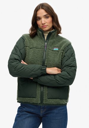 Groene geïsoleerde jas met gequiltte stof en pluizige fleece-textuur. Voorzien van een ritssluiting aan de voorkant, elastische manchetten en een logo-patch op de borst.