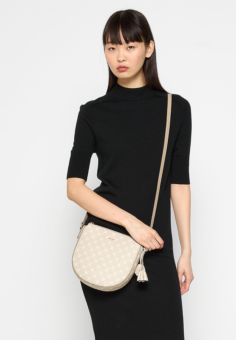 Beige Leder Crossbody-Tasche mit halbkreisförmigem Design, gemusterter Oberfläche, goldfarbenen Beschlägen und einem Quastenakzent.