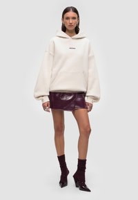 Felpa cremosa oversize con tasca frontale, abbinata a una mini gonna viola lucida. Completata con calze viola a coste e tacchi.