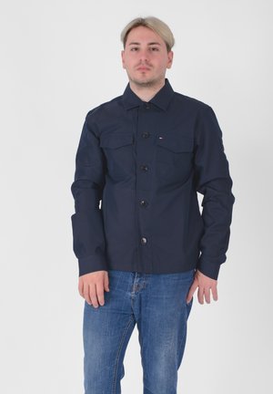 Giacca button-up blu navy con due tasche sul petto; realizzata in un tessuto liscio; presenta un colletto classico e maniche lunghe.