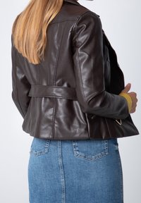 Ruskea nahkatakki, jossa on istuva malli, vyötärönauha ja olkapään epauletit. Yhdistetty vaaleansiniseen denimhameeseen.