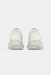 White athletic shoes with textured mesh upper, rubber soles, and "S" logo in rose gold on the heel; sleek design with minimal accents.