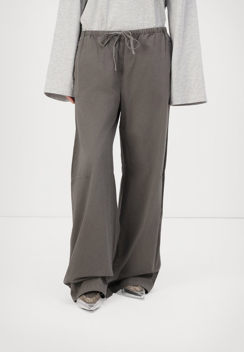 Pantalons larges à taille élastique en tissu gris foncé avec une texture lisse. Présente une fermeture à cordon et une coupe décontractée pour le confort.