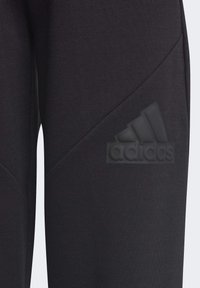 Joggers negros hechos de un tejido texturizado con un diseño diagonal, con un logo de Adidas negro mate en el costado.
