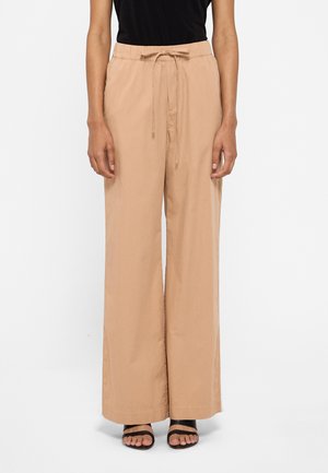 Palazzo pants in beige, featuring a drawstring waist, wide legs, and a smooth texture, paired with black heeled sandals.