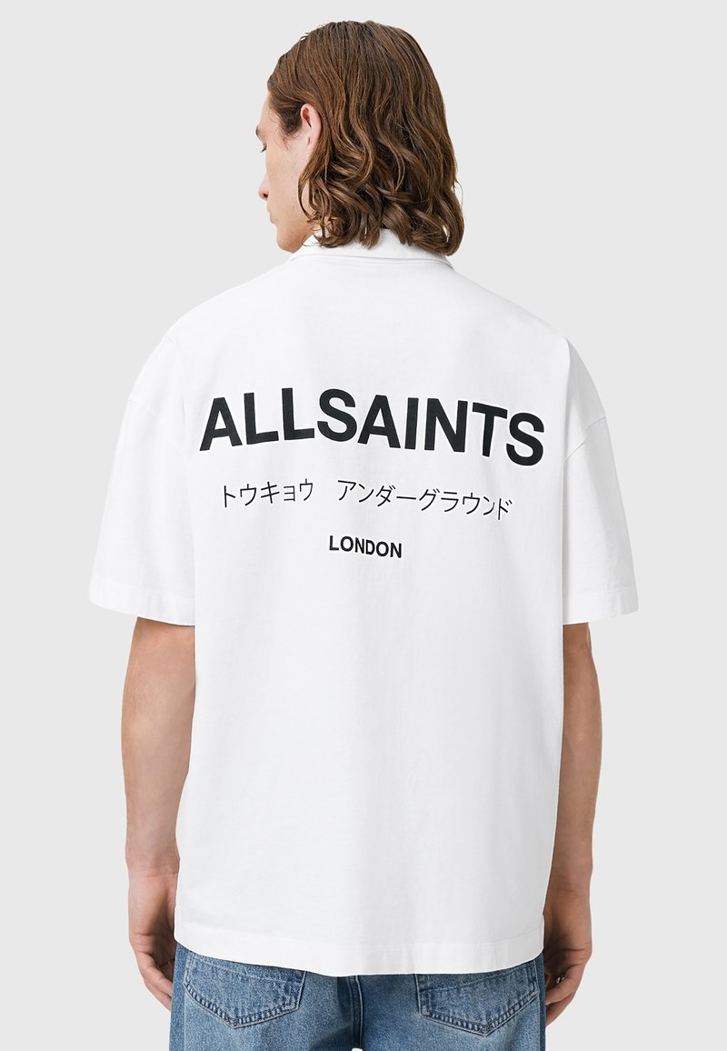 Hvit kortermet T-skjorte med stor svart trykk "ALLSAINTS" og tilleggstekst på japansk, med en avslappet passform og bomullsstoff.