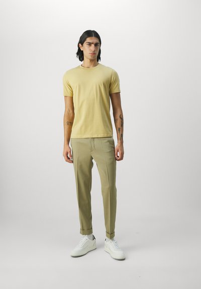 Camiseta amarilla de manga corta combinada con pantalones tapered beige y zapatillas blancas. El conjunto tiene un diseño minimalista y moderno.